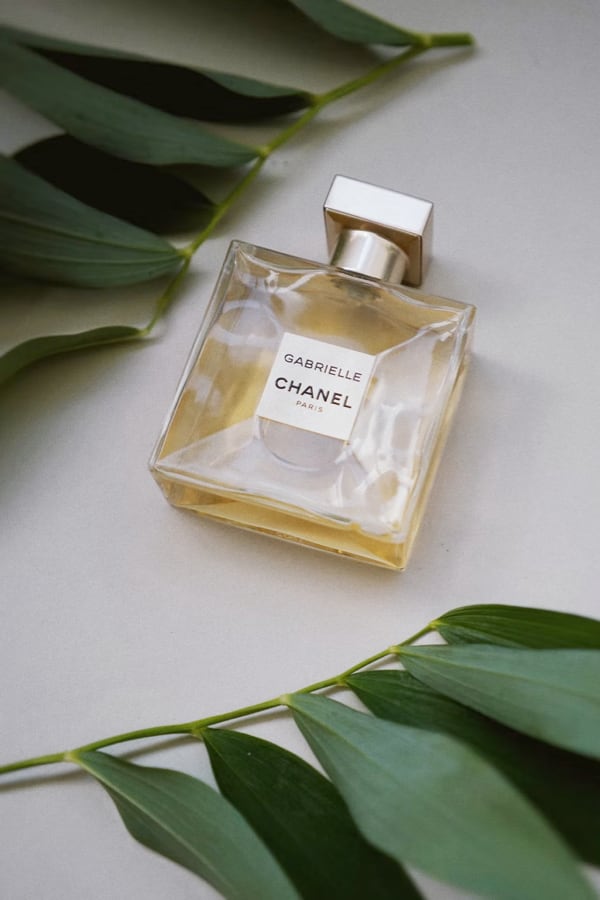 a bottle of perfume on a white table amongst leaves