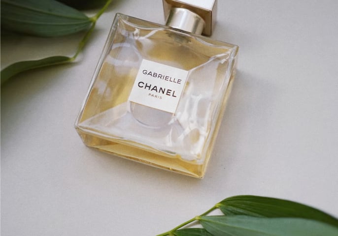 a bottle of perfume on a white table amongst leaves